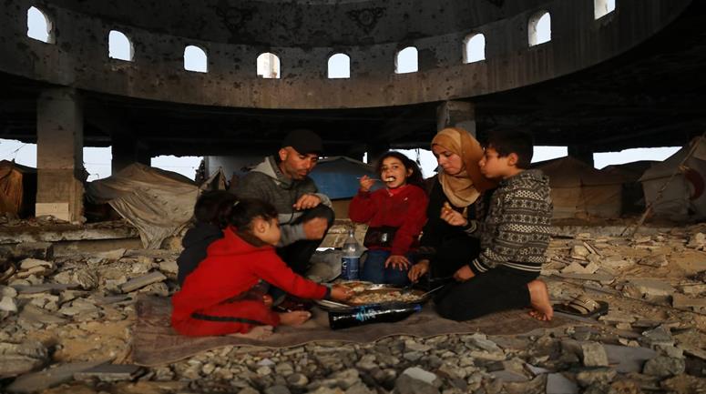عائلة نازحة من حيّ الزيتون تتناول الإفطار فوق ركام مسجد الشافعي في عسقولة شرق غزة، بعد أن أصبح مأوى لها عقب تدمير منزلها في الحرب